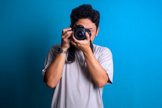 Young professional photographer in red shirt take picture of you using camera on blue background