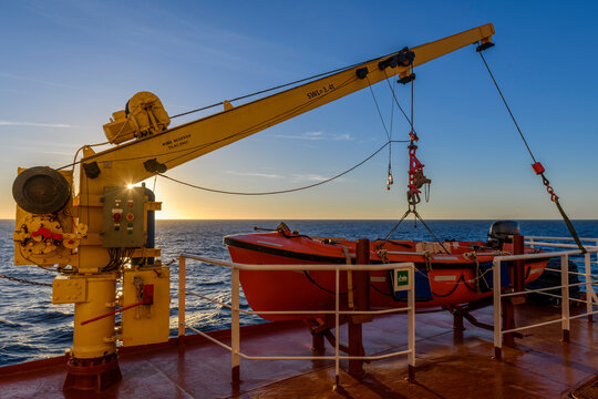 Orange rescue boat on big cargo vessel and crane. Man over board drill. Lifeboat training.