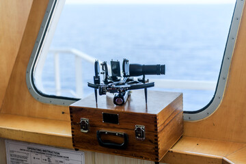 Nautical black sextant placed on wooden box in navigational bridge. Navigational equipment. Celestial navigation.