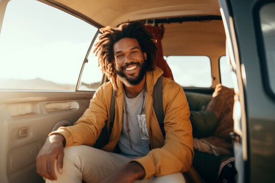 Smiling man with afro hairstyle sitting in his car on a sunny day.