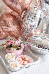 Flowers and sweets on white table and balloons on the white bed. Gift for Valentine's day or March 8 or Mother's Day or birthday