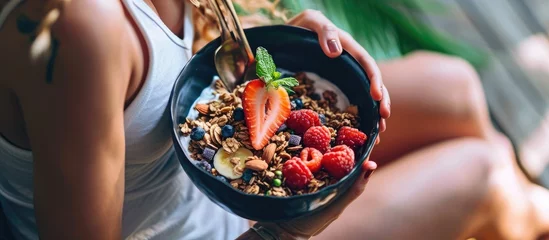 Muurstickers Athlete enjoying healthy meal rich in fiber protein and vitamins Fit young man sitting on floor in living room relaxing after fitness workout eating natural vegetarian granola listening to musi © vxnaghiyev