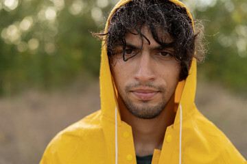 Portrait of a muslim young wet man in a raincoat in the rain, close-up. Bad weather pessimism...