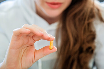 Close-up of a young woman holding a pill capsule in her hand.