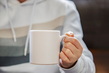 Close up of female hands holding white cup of hot drink. Focus on mug, copy space