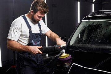 Side view on concentrated professional car service male worker with orbital polisher, polishing...