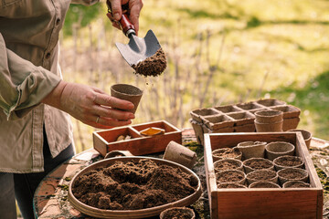 Spring gardening. Female gardener with shovel putting soil and compost into biodegradable peat...