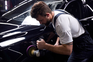Side view on young man auto mechanic worker polishing car at automobile repair and renew service station shop by power buffer machine. Copy Space - obrazy, fototapety, plakaty