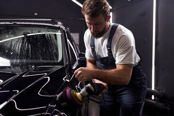 professional car service male worker use orbital polisher, polishing black car in auto repair shop,...