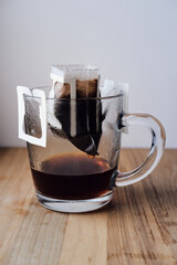 drip coffee with ground black Arabica coffee in a large glass cup close-up. portion of drip coffee per cup. a cup with paper drip coffee stands on a wooden board on a white background close-up.