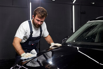 Worker in uniform saw scratch on paint surface of car, polishing and repairing damage using rag in renew service station shop. repair man at work place