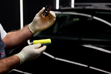 close-up hands applying oil from small jar to rag to clean the surface of auto, in repair and renew...