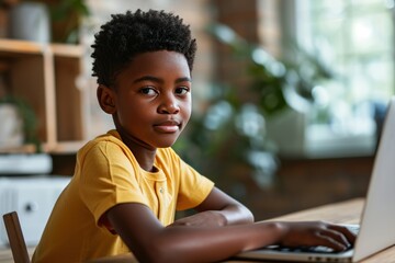 African American boy sitting at the table, look at the camera using the laptop for online lesson learning