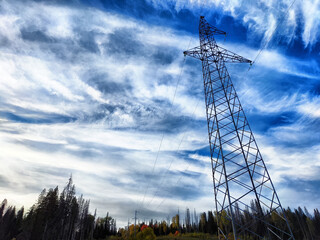 Power lines on a hill, hill or in the mountains against a blue sky with white clouds. Electric lines, towers, wires in the landscape