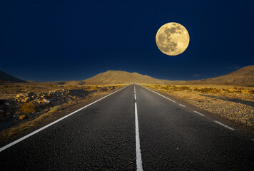  A scenic road with mountains, full moon, and night sky.
