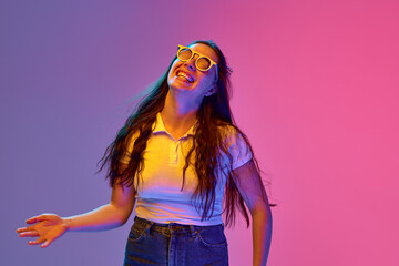 Portrait of positive, charming young brunette woman in sunglasses smiling an laughing against gradient background in neon light. Concept of beauty, and fashion, youth, human emotions, self-expression.