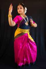 Indian classical dancer in traditional costume performing Bharatanatyam dance mudra on black background
