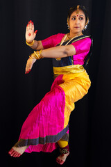 Woman Indian classical dancer in traditional costume performing Bharatanatyam dance on black background
