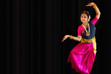 Beautiful Indian classical dancer in traditional costume performing Bharatanatyam dance on black background