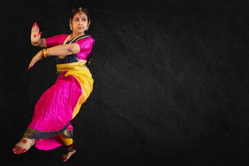 Traditional female Indian classical dancer performing Bharatanatyam on black background with writing space