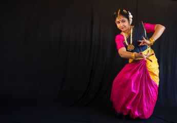 Female Indian classical dancer in traditional costume performing Bharatanatyam dance on black background with writing space