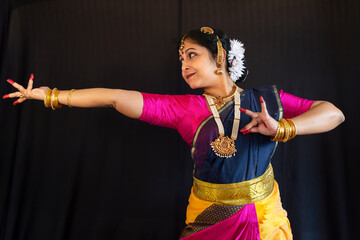 A woman dancer perform the Indian classical dance Bharatanatyam on black background