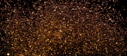 Ground Coffee roasted powder dust fly explosion, Coffee crushed ground float pouring. Roasted Coffee powder ground dust splash explosion in mid Air. Black background Isolated gold bokeh