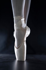 detail of female ballet dancer's feet in ballet position with pointe shoe in front of dark...