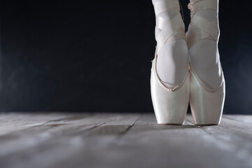detail of female ballet dancer's feet in ballet position with pointe shoe in front of dark background with free space on the left side
