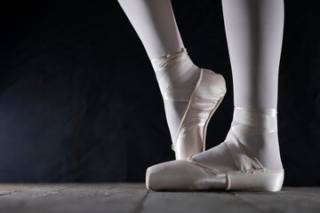 detail of female ballet dancer's feet in ballet position with pointe shoe in front of dark background with free space on the left side