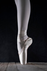 detail of female ballet dancer's foot in ballet position with pointe shoe in front of dark background 