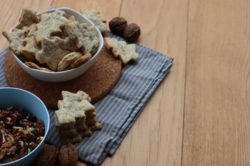 Walnut cookies in shape of a tree ina white bowl with dry walnuts on woooden table 