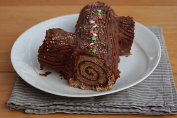 Close-up of a chocolate yule log filled with chestnut cream on a plate on  wooden table. Traditional festive Buche de Noel