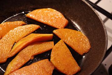 Frying pan with tasty roasted pumpkin pieces on the stove