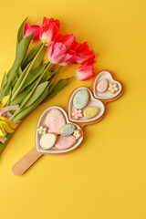 Obraz na płótnie Canvas Sweets, pastry, gingerbread cookies for Easter table. Easter eggs heart shaped decor plate, pink tulips on yellow background top view copy space, spring seasonal holiday banner for site, flyer, coupon