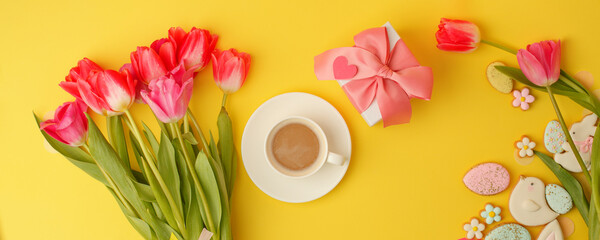 Easter gingerbread cookies, spring flowers, cup of coffee on yellow background. Cozy home Easter greeeting card concept, banner for your site, copy space top view, stylish composition