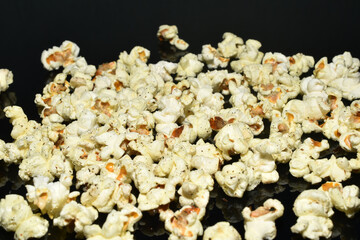 Popcorn lies in a pile on a dark background.