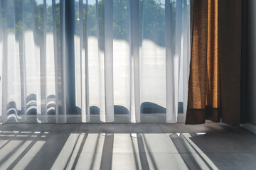 Sun rays penetrate the room through transparent white curtain tulle