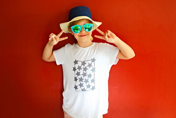 Pretty emothional child wear a hat and sunglasses on a red background