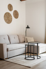 Vertical shot of a beige style corner sofa stands on the floor with a coffee table and circle wall decor and a floor lamp. Concept of a modern living room in a new building