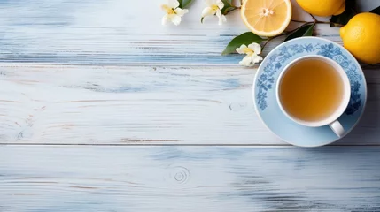 Poster A cup of hot green fragrant tea with lemon and jasmine on a light blue wooden table, a warm cozy atmosphere. Top view, copy space background. © Nikolai
