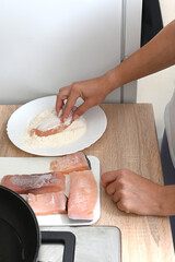 Women's hands roll pieces of fish in flour and egg batter