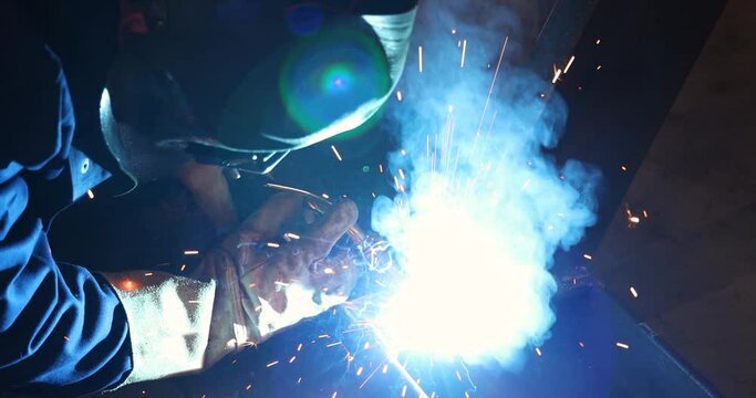Welder at work in metal industry, welding metal construction - slow motion. Close-up shot lots of sparks in the factory