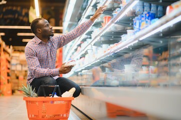 Portrait of smiling man at supermarket. Young african man with shopping basket in grocery store