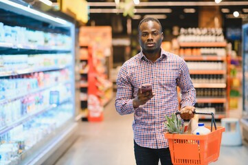 Portrait of smiling man at supermarket. Young african man with shopping basket in grocery store