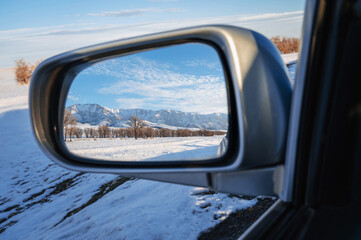 beautiful winter landscape with Tien Shan mountains and trees in field in the snow in rearview mirror of car. Concept of festive holiday winter travel in Kazakhstan