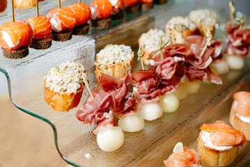 Assorted Gourmet Canapes on Glass Serving Tray. A luxurious array of gourmet canapes, including melon with prosciutto and smoked salmon on pumpernickel, presented on a chic glass serving tray.