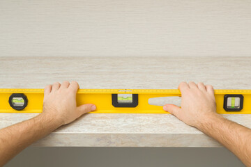 Young adult man hand using yellow spirit level and measuring horizontal surface of beige stone tabletop. Assembling new kitchen furniture. Closeup. Point of view shot. Renovation process.