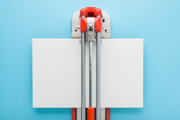 Manual cutter with new white ceramic tile on light blue table background. Pastel color. Preparing...