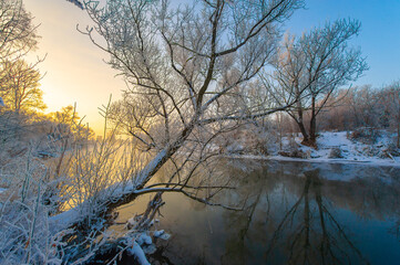 Naklejka na ściany i meble Enjoy the stunning beauty of nature's colors at sunrise. See how the sun illuminates the icy river with warm light. Be enchanted by the breathtaking spectacle of winter magic.